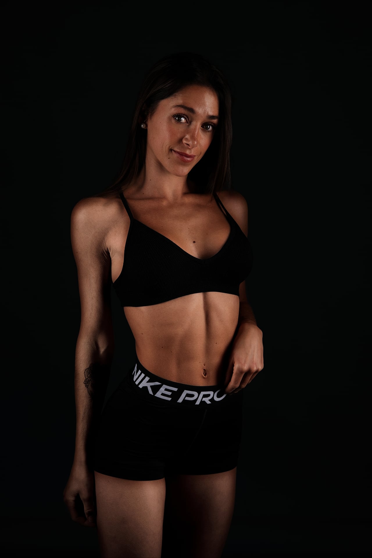 La Marta, de mig cos, dreta amb top esportiu negre i pantaló curt, abdominals marcats, sobre fons negre d'estudi.